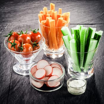 Serving of fresh vegetable crudites on a buffet with individual glass containers of carrot and cucumber batons, sliced radish and cherry tomato with a vinaigrette dip