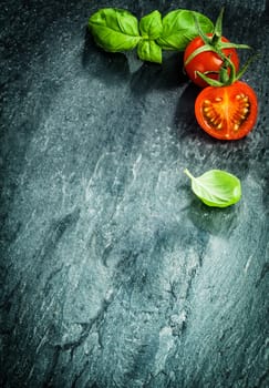 Fresh cooking ingredients with basil and tomato forming a corner border on a darked cracked and texture surface with copyspace and vignetting