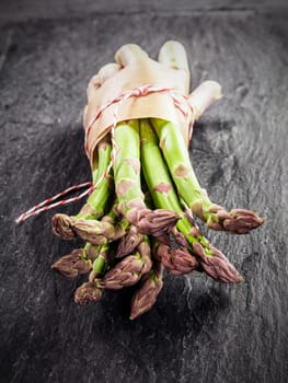 Fresh green asparagus spears bundled in brown paper and tied with string displayed with their tips to the camera on a grey textured slate surface