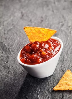 Spicy hot tomato and chili salsa dip in a small white ceramic bowl with a corn totilla for a tasty savory appetizer or snack