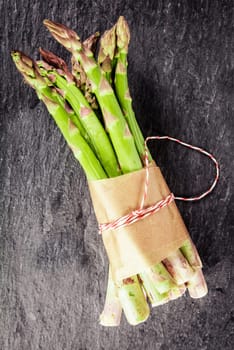 Fresh green asparagus spears tied in a brown paper wrapper for a healthy vegetarian cuisine lying on a grey slate surface, overhead view