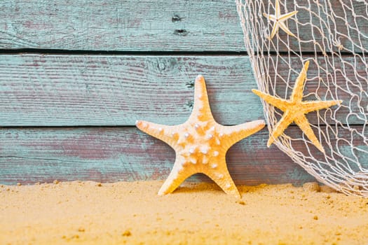 Nautical background with starfish and a fishing net against rustic weathered blue wooden planks above golden beach sand