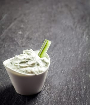 Delicious creamy vinaigrette and cottage cheese sauce in a ceramic dish with a cucumber crudites or baton for a healthy snack or appetizer on grey slate with copyspace