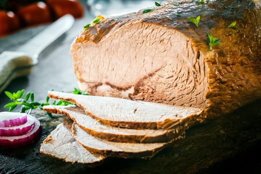 Close up of a savory sliced German meat loaf roasted in a casserole and seasoned with fresh herbs on a wooden chopping board