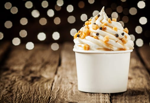 Delicious frozen yogurt party dessert twirled in a tub and decorated with sprinkles against a sparkling bokeh of festive lights