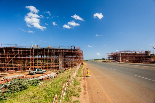 New bridge construction over road highway with building materials and machines on roadside site.