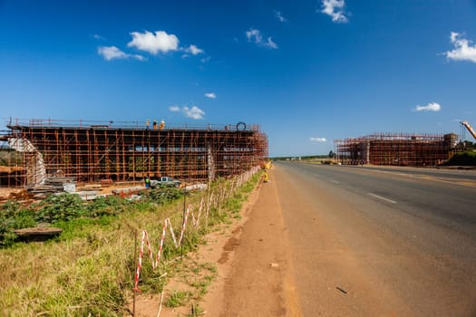 New bridge construction over road highway with building materials and machines on roadside site.