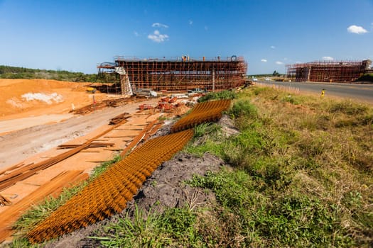 New bridge construction over road highway with building materials and machines on roadside site.