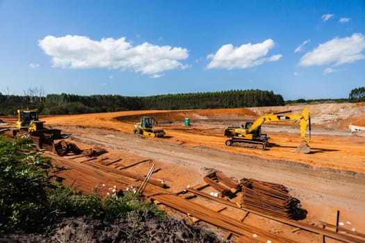 New bridge construction over road highway with building materials and machines on roadside site.