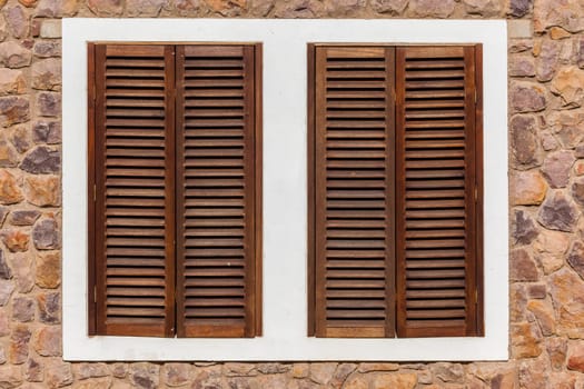 Windows in stone wall of home with wood shutters for weather,privacy and security
