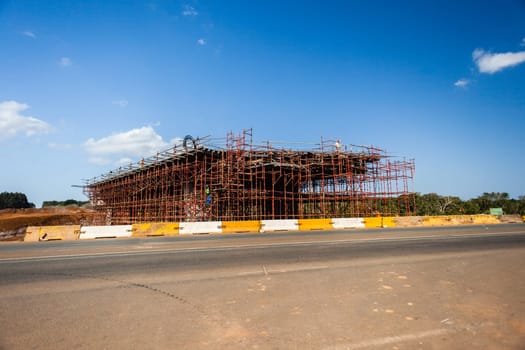 New bridge construction over road highway with building materials and machines on roadside site.