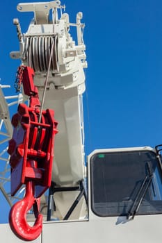 Mobile crane vehicles red hoist hook and white painted extension arms and operator cabin on vehicle against blue sky