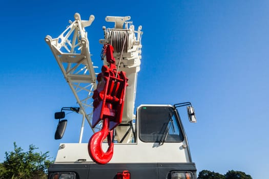 Mobile crane vehicles red hoist hook and white painted extension arms and operator cabin on vehicle against blue sky