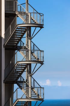 Building section back metal stairway fire-escape exit overlooking blue ocean.