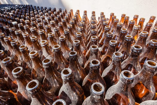 Glass bottles stacked outdoors alongside wall gathering dust in detail, close overhead photo image.