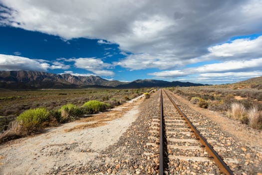 Rail track single line travels over the rugged rural wilderness landscape plateau nearby distant mountains