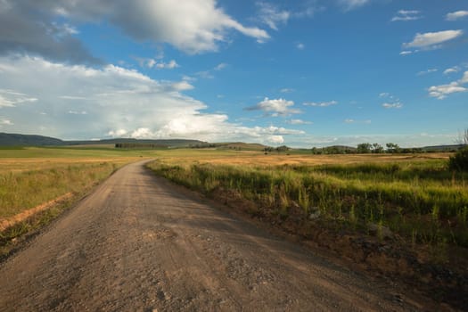 Dirt road through summer mountains fields and hills late afternoon color