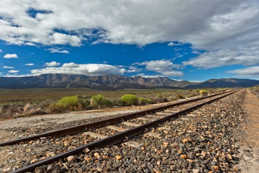 Rail track single line travels over the rugged rural wilderness landscape plateau nearby distant mountains
