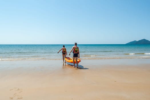 Couple man woman unidentified carrying kayak into tropical waters at  mission beach nearby Cairns Queensland Australia