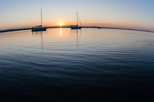 Scenic sunset landscape over river lagoon estuary waters with two silhouetted yachts on glass smooth waters