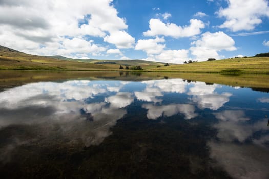 Small mountain lake dam with glass mirror reflections of clouds and blue sky over scenic beauty landscape