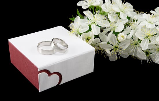 White gold wedding rings on the box with flowers isolated on black
