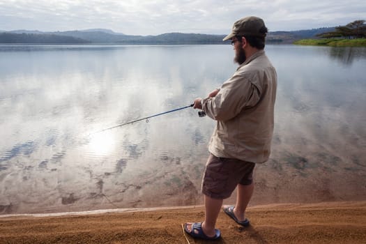 Fisherman closeup fishing on smooth glass dam waters landscape