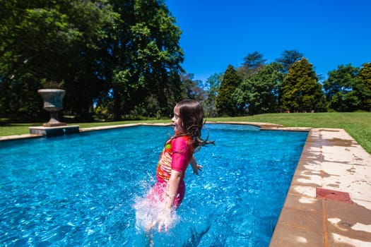 Girl at home playtime jumping into swimming pool outdoors summer