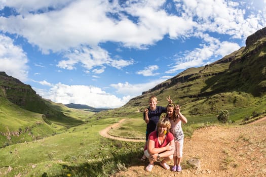 Family on explore adventure on 4x4 dirt road winding through mountain pass over scenic terrain on a summer blue day with cloud puffs