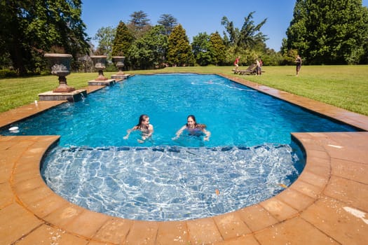 Teen girls in swimming pool with boys on grass lawn outdoors summer