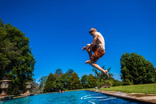 Teenager boy jumping into swimming pool outdoors summer