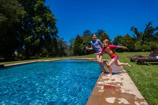 Girls at home playtime jumping into swimming pool outdoors summer