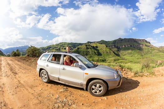 Family travel explore adventure on 4x4 dirt road winding through mountain pass over scenic terrain on a summer blue day with cloud puffs