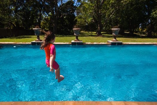 Girl at home playtime jumping into swimming pool outdoors summer