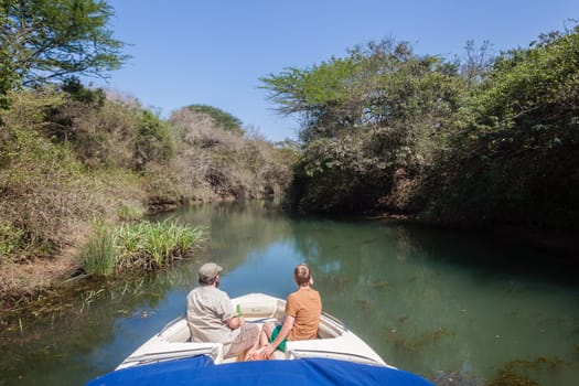Ski-Boat with two men looking, exploring dam river tributary channel on dam in rural wilderness terrain.