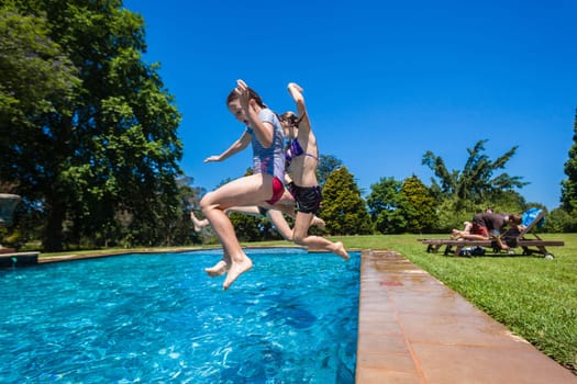 Girls cousins teenagers at home playtime jumping into swimming pool outdoors summer