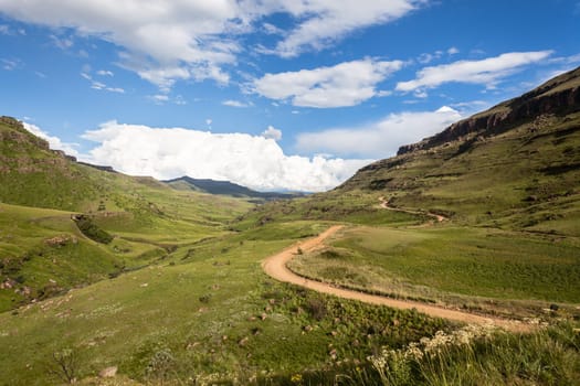 Dirt road winding through mountain pass over scenic terrain on a summer blue day with cloud puffs
