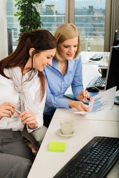 Young businesswomen discussing graph at office desk