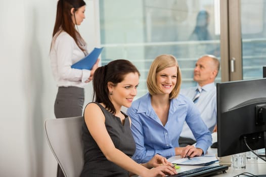 Businesswomen using computer with colleagues in background at office