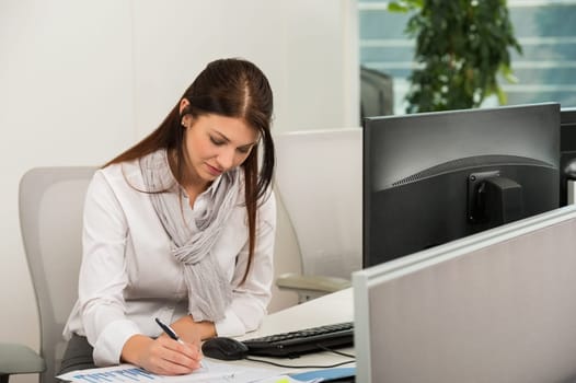Businesswoman sitting while writing at computer desk