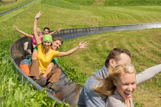 Excited young couples enjoying alpine coaster luge during summer