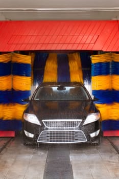 Car being washed in automatic car wash,rotating blue and yellow brushes visible  Unrecognizible make and model labels,model release not required.