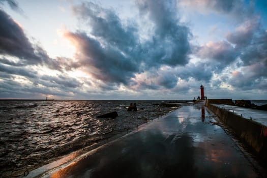 fragment of concrete,wet of rain breakwater with visible raugh sea,dramatic sun set and clouds,visible storm lantern,lighthouse.
