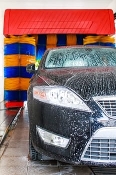 car being washed in automatic car wash,blue and yellow rotating brushes visible  unrecognizible make and model labels,model release not required.