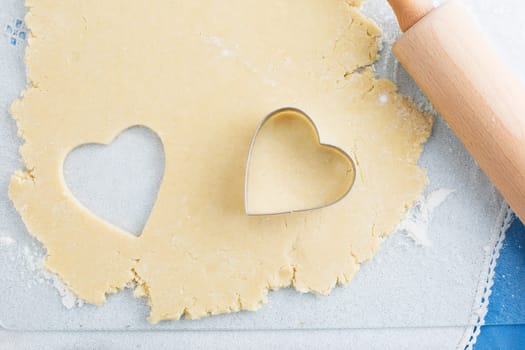 Heart shaped cookie cut out of cookie dough with cutter and rolling pin