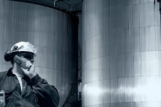 oil and gas industrial fuel storage tanks inside refinery, engineer, worker talkin in phone