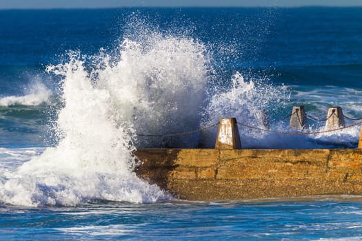 Ocean waves crashing breaking on shallow reefs and washing along beach coastline into concrete tidal pool with power and energy of nature