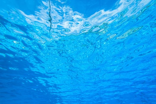 Underwater swimming pool waters towards surface and blue sky
