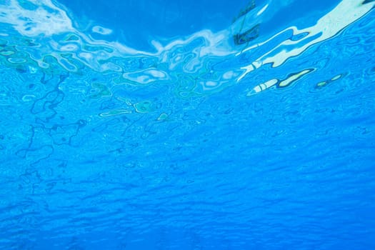 Underwater swimming pool waters towards surface and blue sky