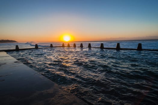 Ocean waves crashing breaking on shallow reefs and washing along beach coastline into concrete tidal pool with power and energy of nature